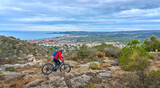 Fototapeta Natura - activ senior woman riding her electric mountain bike on the cliffs above the city of Denia, Costa Blanca, Spain, Europe