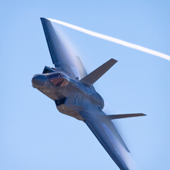 Wall Mural - Close view of a F-35C Lightning II  approaching in a high G maneuver, with condensation clouds over the wings, trails at the wing tips and afterburner on