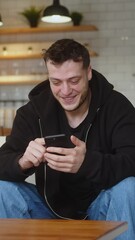 Vertical video. Smiling man sitting on couch using smartphone check message read notice receive good news on e-mail celebrate great opportunity feels happy	
