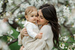 © Алина Троева - Woman mother holds hugs adorable baby at nature blossom, Mother's Day concept.
