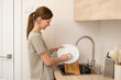 A girl washes dishes in a bright cosy kitchen. A young woman cleans up after dinner.