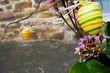 Osterdekoration mit bunten Eiern aus Holz an Strauß vor grauem Gehweg und alter braun-grauer Backsteinmauer in Stadt am Nachmittag im Frühling