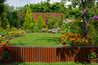 zielony trawnik w ogrodzie otoczony krzewami ozodbnymi i kolorowymi kwiatami, beautiful garden with shrubs, lily, marigold and conifers, designer garden	