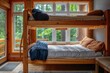 © At My Hat - A wooden bunk bed with a blue blanket and a white comforter. The bed is in a room with a view of trees