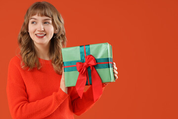 Poster - Beautiful young woman with gift box on orange background