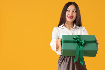 Poster - Beautiful young Asian woman with gift box on yellow background