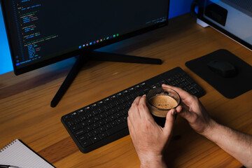 programmer drinking coffee at wooden desk