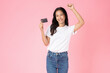 Cheerful beautiful Asian woman holding mockup credit card isolated on pink background.