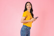 Beautiful Asian woman holding smartphone and smiling on pink background.