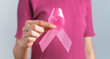 Woman hand holding pink ribbon for breast cancer patients and survivors, World cancer day concept.