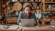 In his spacious workshop filled with construction tools, a young bearded craftsman is leaning over a workbench and using a laptop to browse the internet.