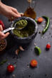 woman mixing green sauce in a stone marble mortar
