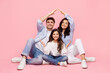 © Home-stock - Cheerful mom dad and girl move new house, parents making roof sign, posing isolated over pink color background