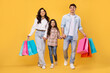 © Home-stock - Happy cheerful parents and their daughter with bright shopping bags walking on yellow background, enjoying seasonal sales and promos
