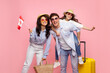 Family vacation. Happy family of three travelling together, woman holding Canada flag, posing with suitcase on pink background