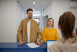 Fototapeta Tęcza - Happy man and woman couple signing document at modern clinic reception desk