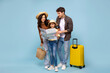 © Home-stock - Happy family with daughter looking at map, planning travel, standing with suitcase on blue studio background, ready for summer vacation