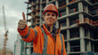A Caucasian female construction worker in a hard hat gives a thumbs up against the background of a building under construction. The concept of safety at the construction site. Work in construction 