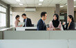 Asian man and two women office employee working on digital tablet PC while standing in open space office with blurred colleagues working on laptop in background