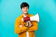 Young Russian man isolated on blue background holding a megaphone and smiling