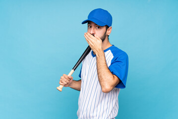 Wall Mural - Young man playing baseball over isolated blue background covering mouth with hands