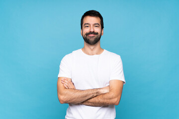 Wall Mural - Young man with beard  over isolated blue background keeping the arms crossed in frontal position
