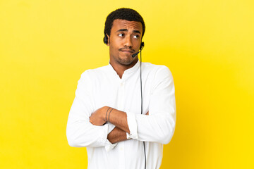 Wall Mural - African American Telemarketer man working with a headset over isolated yellow background making doubts gesture while lifting the shoulders