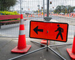 Man Walking Road sign in front of a closed footpath. Traffic cones and fences along the road. Roadworks in Auckland.