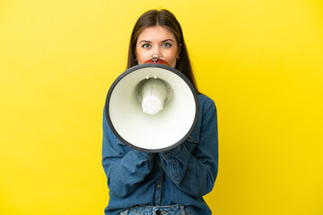 Wall Mural - Young caucasian woman isolated on yellow background shouting through a megaphone to announce something