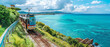 A tram winds along a picturesque coastal road, surrounded by lush greenery and blue waters.