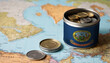A jar filled with cash, displaying the Idaho flag, sits atop a map. Saving for vacation, leisure activities. Financial planning, travel budget allocation
