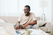 © SHOTPRIME STUDIO - Smiling African American Male Freelancer Working on Laptop in Modern Home Office
