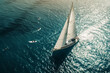 Modern sailboat gliding across the sea with distant swimmers below in a high angle view
