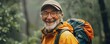 Cheerful older man with a hat smiles in rainy forest. Camping in rain concept