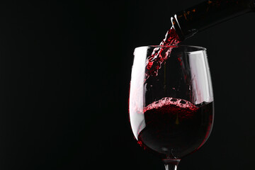 Sticker - Pouring red wine into glass against black background, closeup. Space for text