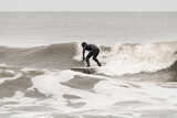 Fototapeta  - Male surfer in a black wetsuit stands confidently on a surfboard, riding a wave