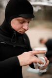 Fototapeta  - Young male surfer wearing a wetsuit scoops up a jar of water repellent cream to apply to his face