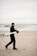 Male surfer walks along the sandy seashore with his surfboard in his hands