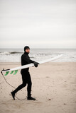 Fototapeta  - Male surfer walks along the sandy seashore with his surfboard in his hands