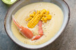 Bowl of corn chowder with crab meat, horizontal shot on a beige granite background, middle close-up