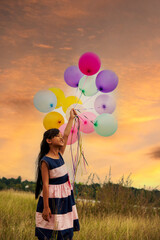 Wall Mural - Vertical sunrise golden vibrant sky hands holding balloons. Cheerful cute girl running on green meadow happiness. Hands holding vibrant air balloons play on birthday party happy gold sky outdoor