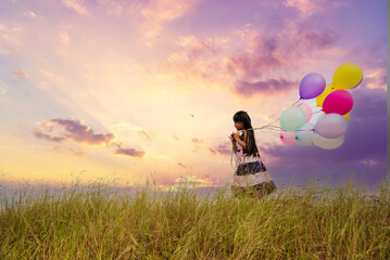 Wall Mural - Cheerful cute girl holding balloons running on green meadow violet purple pastel sky happiness. Hands holding vibrant air balloons play on birthday party happy times summer on pueple sky outdoor