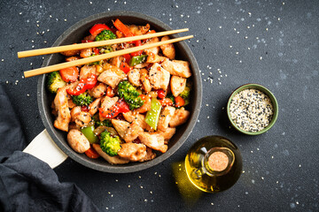 Wall Mural - Stir fry chicken and vegetables and sesame at black background. Asian cuisine. Top view with space for design.