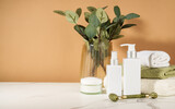 Fototapeta  - Skin care products in the bathroom. Face cream, serum bottle, jade roller and stack of towels.
