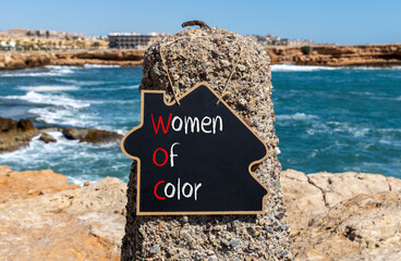 Wall Mural - WOC women of color symbol. Concept words WOC women of color on beautiful yellow blackboard. Beautiful stone blue sky sea background. Business WOC women of color social issues concept. Copy space.