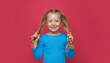 Little cheerful girl plays with her hair on a pink background.