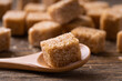 Natural brown sugar cubes on wood background. Brown cane sugar cube in a wooden spoon close up. Sugar cubes.