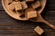 Natural brown sugar cubes on wood background. Cane sugar cubes in a wooden plate on the table.