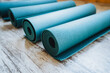 Three azure yoga mats rest on wood floor, rolled up