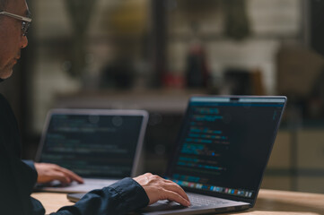Programmer man is typing and coding on a laptop computer. He is wearing glasses and has a hand on the keyboard. The laptop is open and the screen is black. The man is focused on his Homework